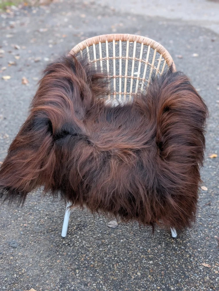 A cozy thick dark rusty icelandic sheepskin throw draped over a woven wicker chair with white metal legs