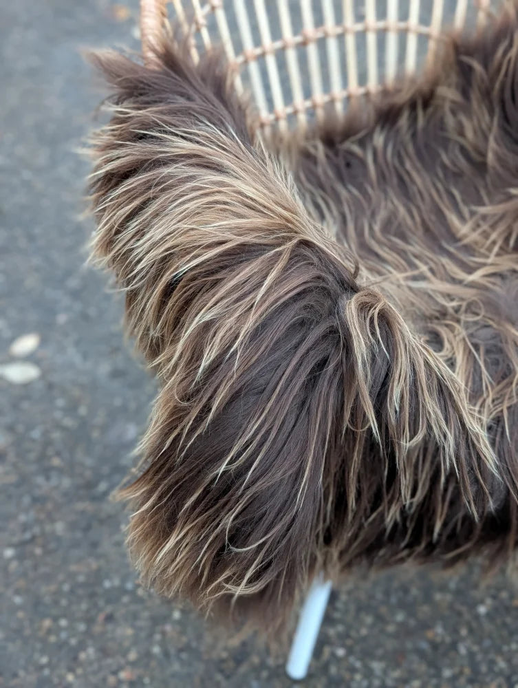 A plush dark rusty icelandic sheepskin throw with long wool draped over a wicker chair for cozy style