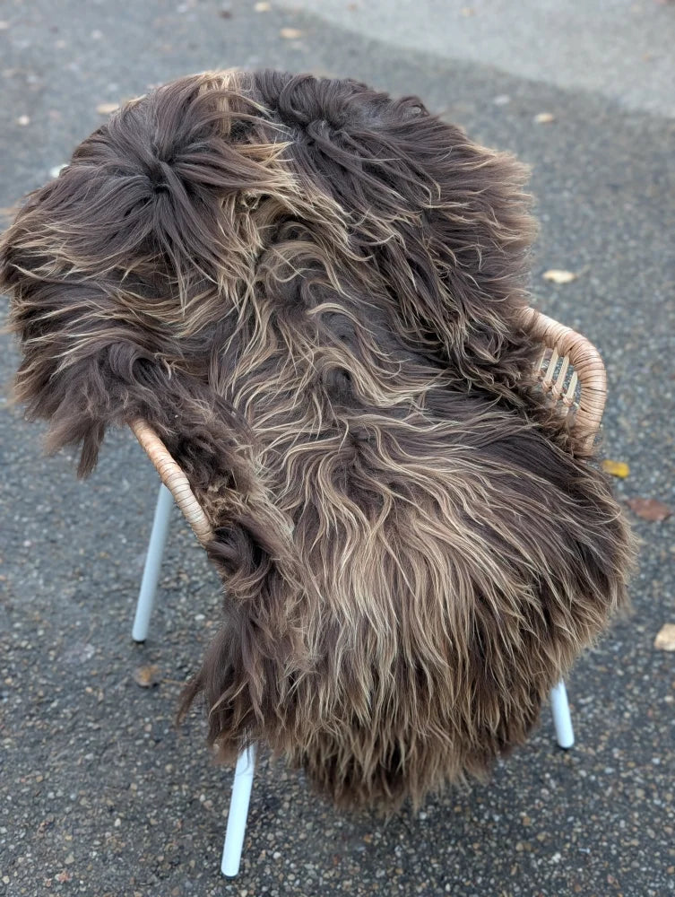 A thick dark rusty icelandic sheepskin rug with long wool draped over a wicker chair with white metal legs