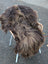 A thick dark rusty icelandic sheepskin rug with long wool draped over a wicker chair with white metal legs