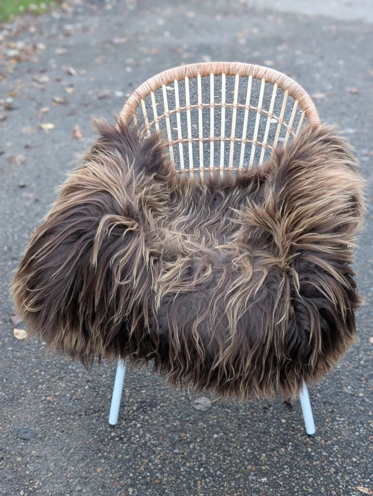 A cozy massive 56 x 35 dark rusty icelandic sheepskin throw with long wool draped over a modern rattan chair