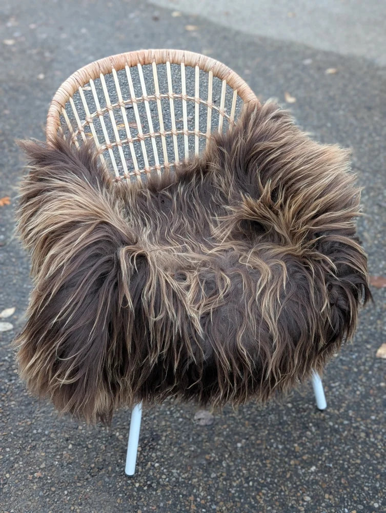 A cozy dark rusty icelandic sheepskin throw with long wool draped over a wicker chair with white metal legs