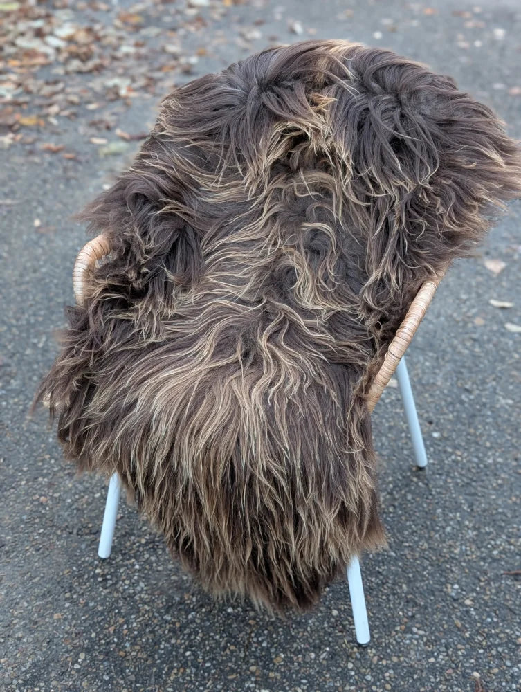 Thick shaggy dark rusty icelandic sheepskin rug with long wool draped over modern chair with light wooden arms