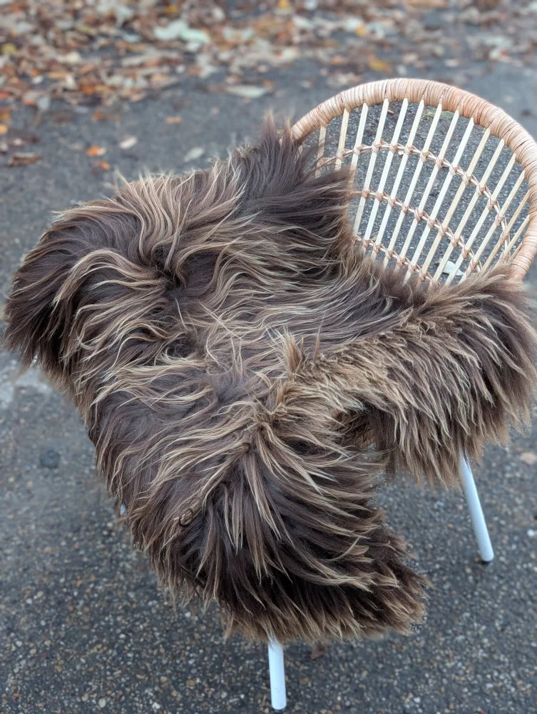 A thick long wool icelandic sheepskin throw in dark rusty bronze draped over a wicker chair with white metal legs