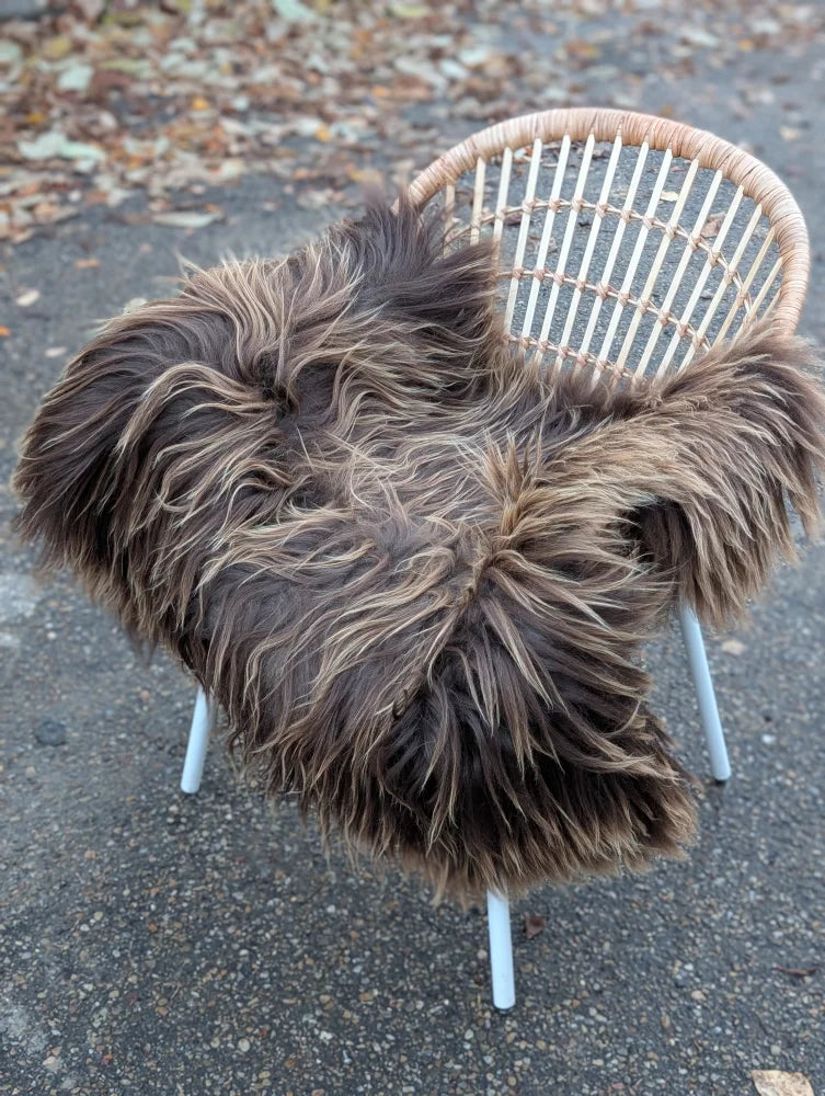 A plush dark rusty icelandic sheepskin throw in long wool draped over a white wicker chair for cozy decor