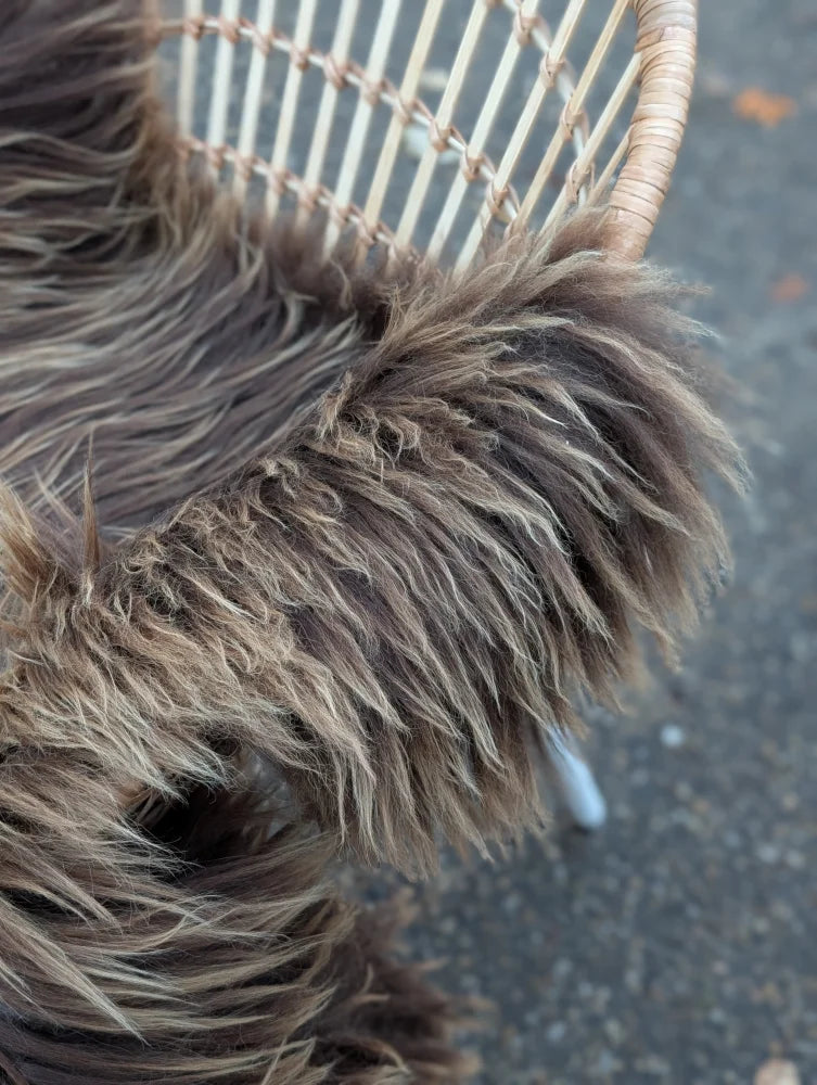 A plush shaggy dark rusty icelandic sheepskin throw draped over a woven wicker chair in bronze tones