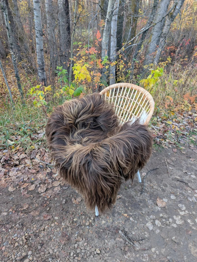 A cozy thick brown faux fur throw draped over a wicker chair showcasing a massive natural bronze icelandic sheepskin