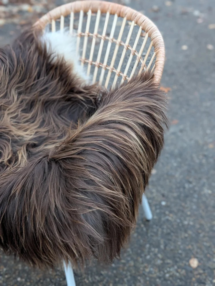 A plush dark rusty icelandic sheepskin throw with long wool icelandic fur draped over a light wicker chair