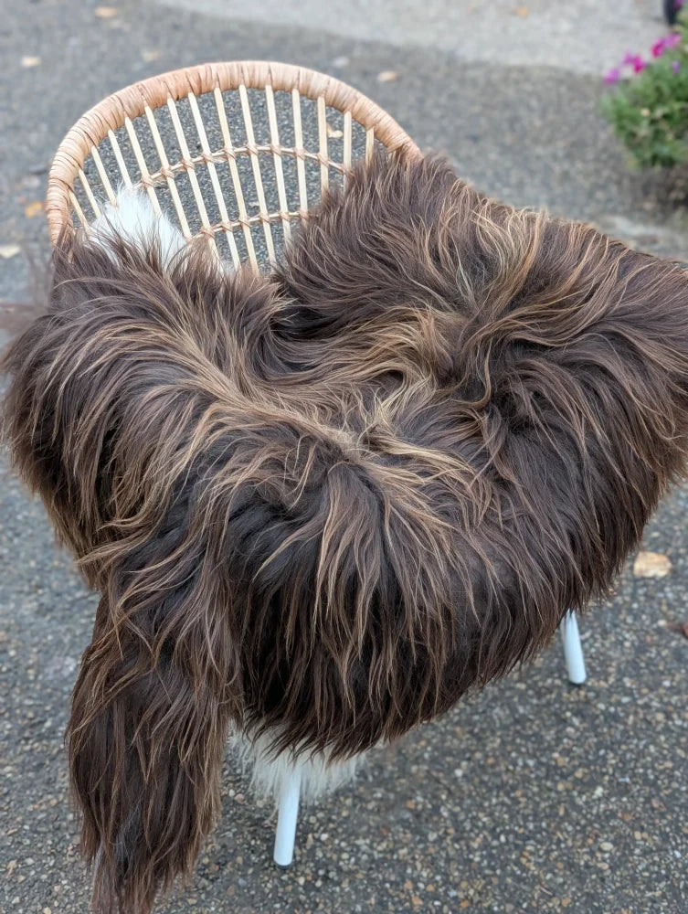 A long wool icelandic sheepskin throw in dark rusty bronze draped over a wicker chair for cozy decor