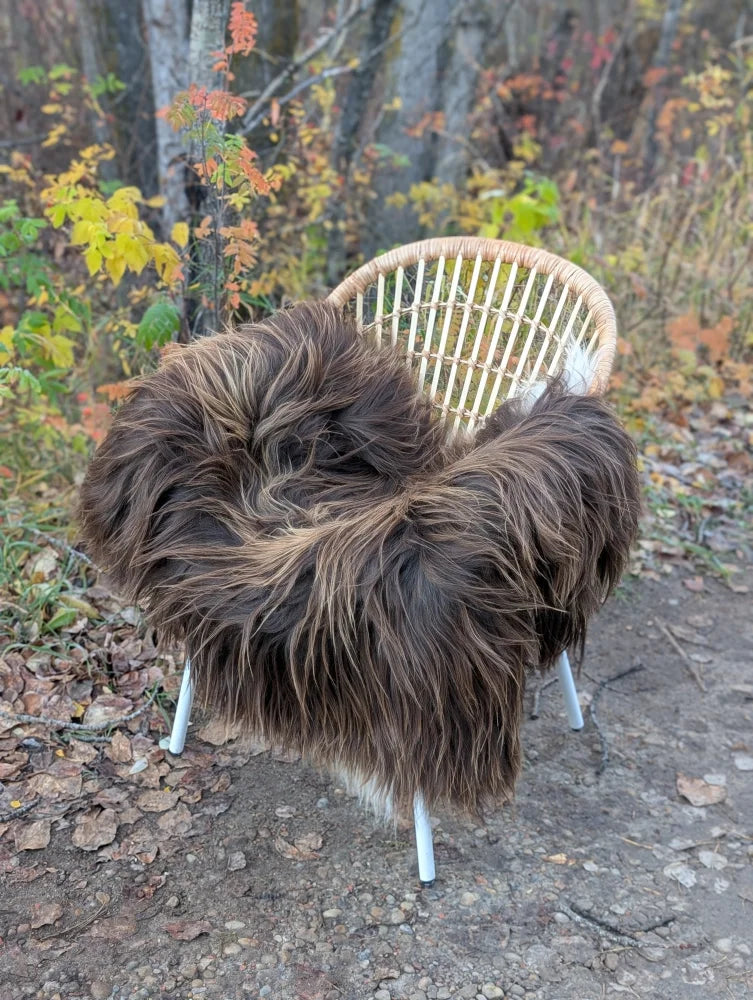 A cozy thick brown faux fur throw draped on a light wicker chair with white legs from ice79 wool icelandic sheepskin