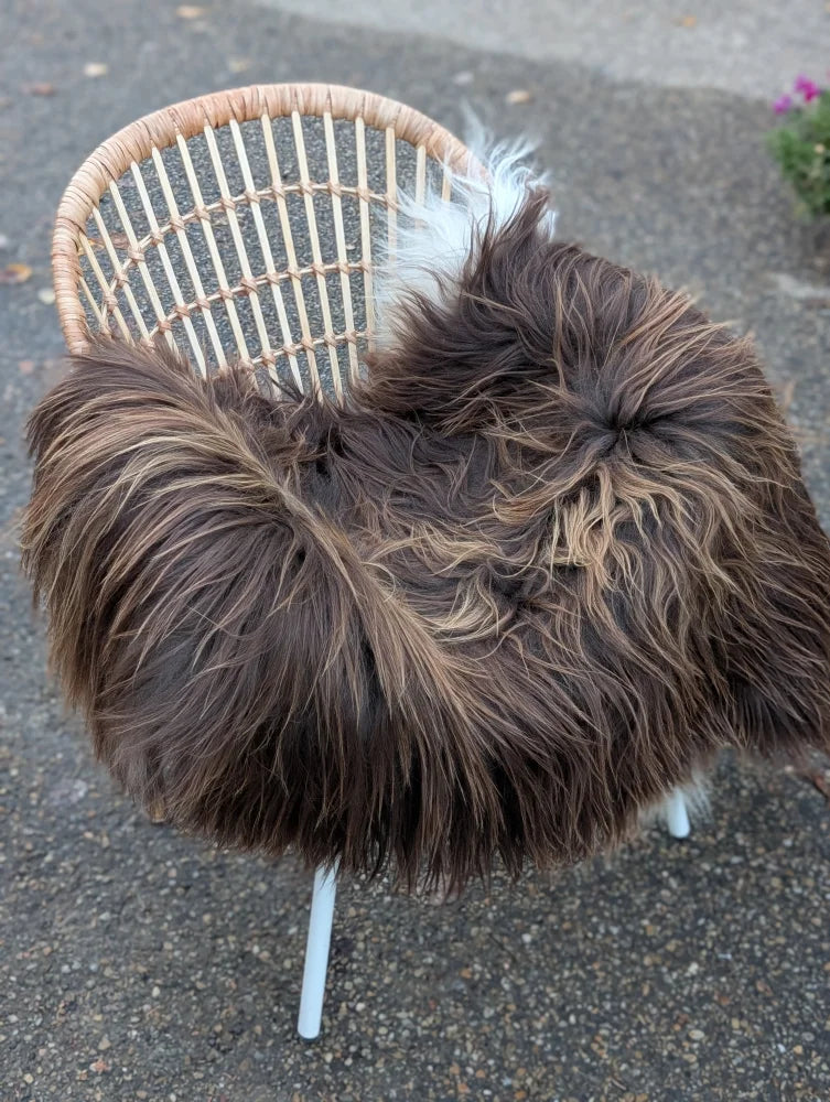 A long wool icelandic sheepskin throw in dark rusty brown draped over a wicker chair with white legs