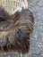 A plush shaggy brown and tan wool icelandic sheepskin throw draped over a wicker chair for cozy use
