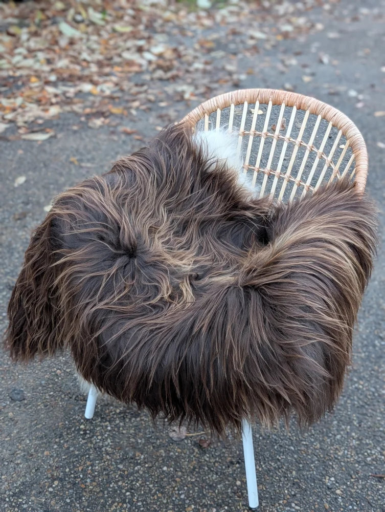 A plush long wool icelandic sheepskin throw in dark rusty icelandic colors draped over a modern wicker chair with white legs