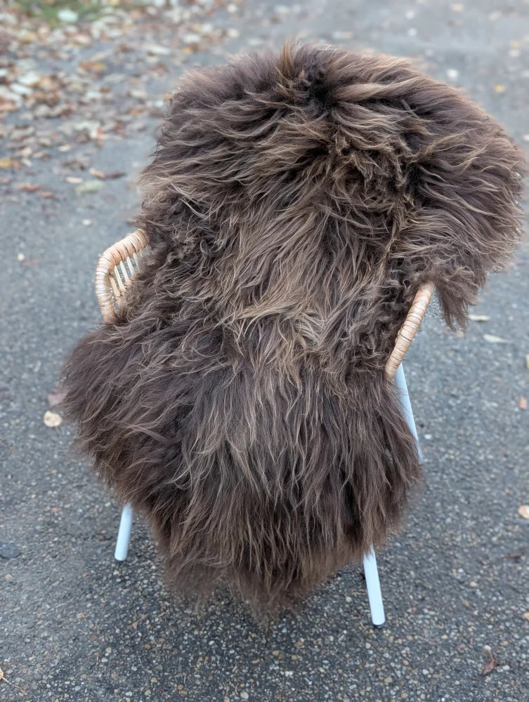Thick shaggy dark rusty icelandic sheepskin rug draped over woven wicker chair in massive natural bronze color