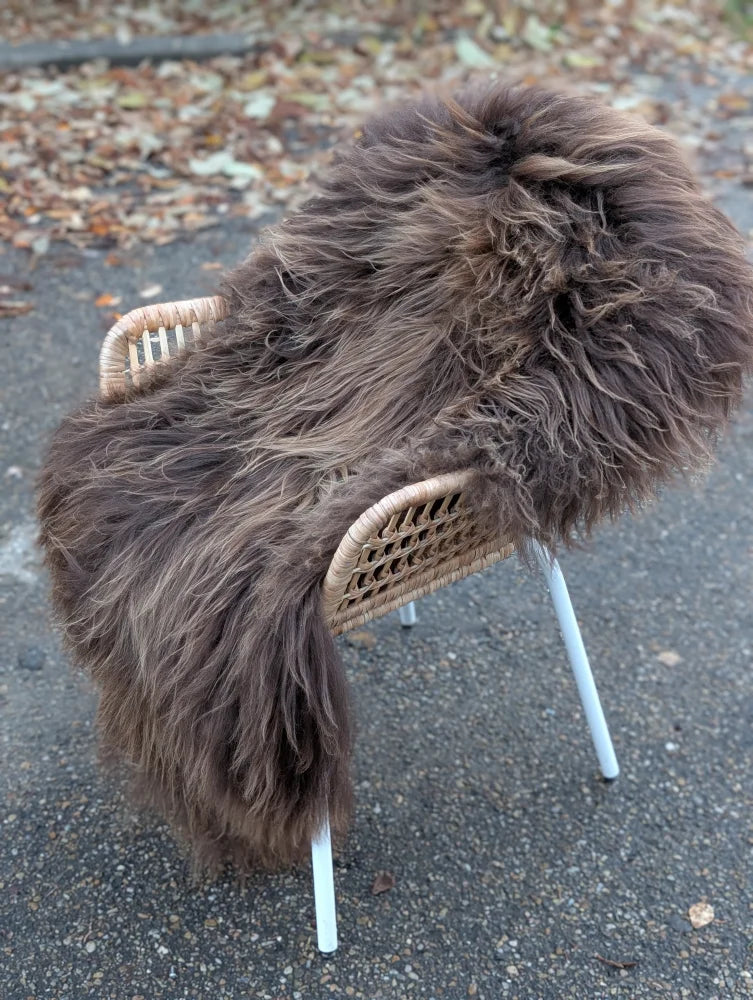 A thick shaggy dark rusty icelandic sheepskin rug draped over a wicker chair with white metal legs