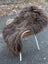 A thick shaggy dark rusty icelandic sheepskin rug draped over a wicker chair with white metal legs