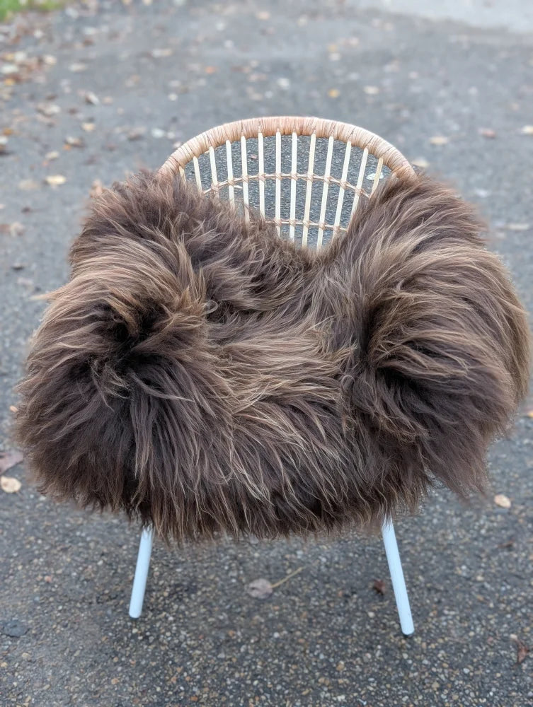 A plush thick dark rusty icelandic sheepskin throw draped over a white metal-framed wicker chair