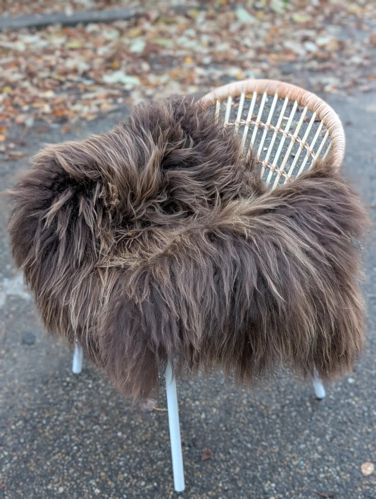 A thick fluffy dark rusty icelandic sheepskin rug draped over a white wicker chair showcasing long wool icelandic texture