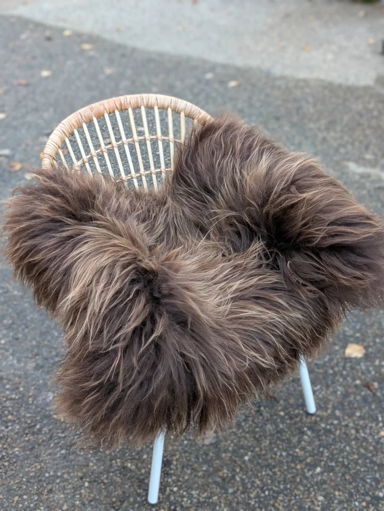 Thick shaggy dark rusty icelandic sheepskin throw draped over woven wicker chair in massive natural bronze color
