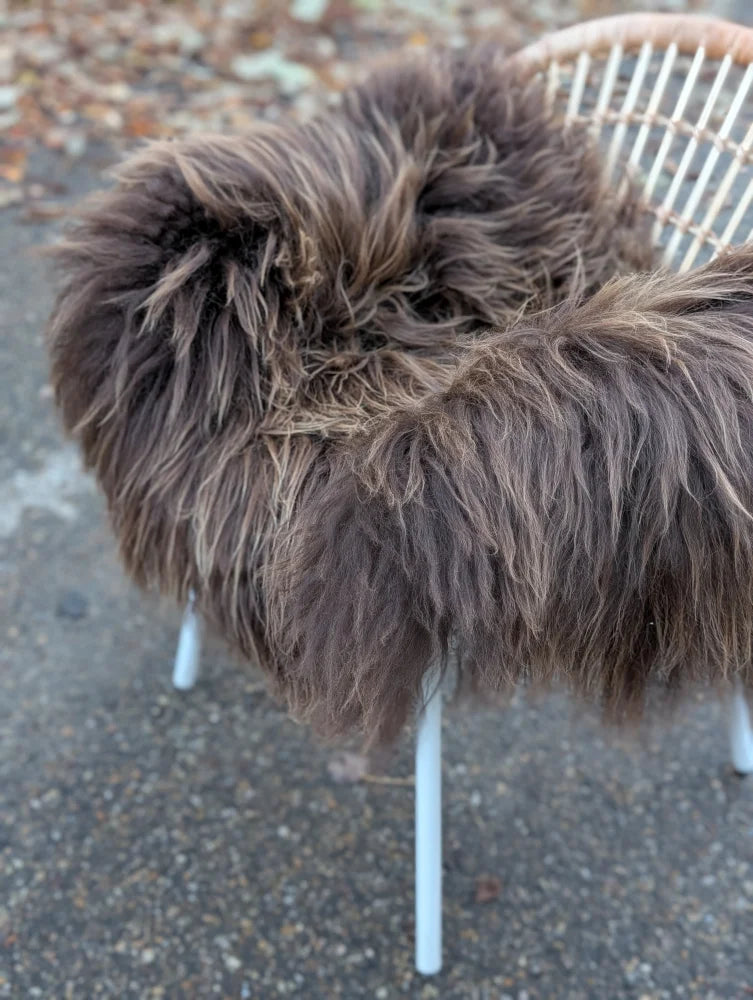 A plush dark rusty icelandic sheepskin throw with long wool draped over a white wicker chair for cozy use