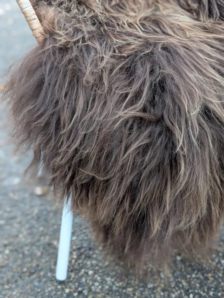 A plush chair with shaggy dark rusty icelandic sheepskin fur, woven wooden backrest, and white legs