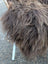 A plush chair with shaggy dark rusty icelandic sheepskin fur, woven wooden backrest, and white legs