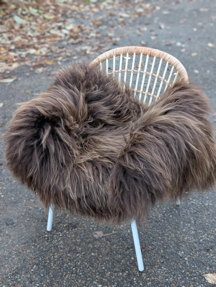 A plush shaggy brown dark rusty icelandic sheepskin throw draped over a white wicker chair for cozy comfort