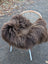 A plush shaggy brown dark rusty icelandic sheepskin throw draped over a white wicker chair for cozy comfort