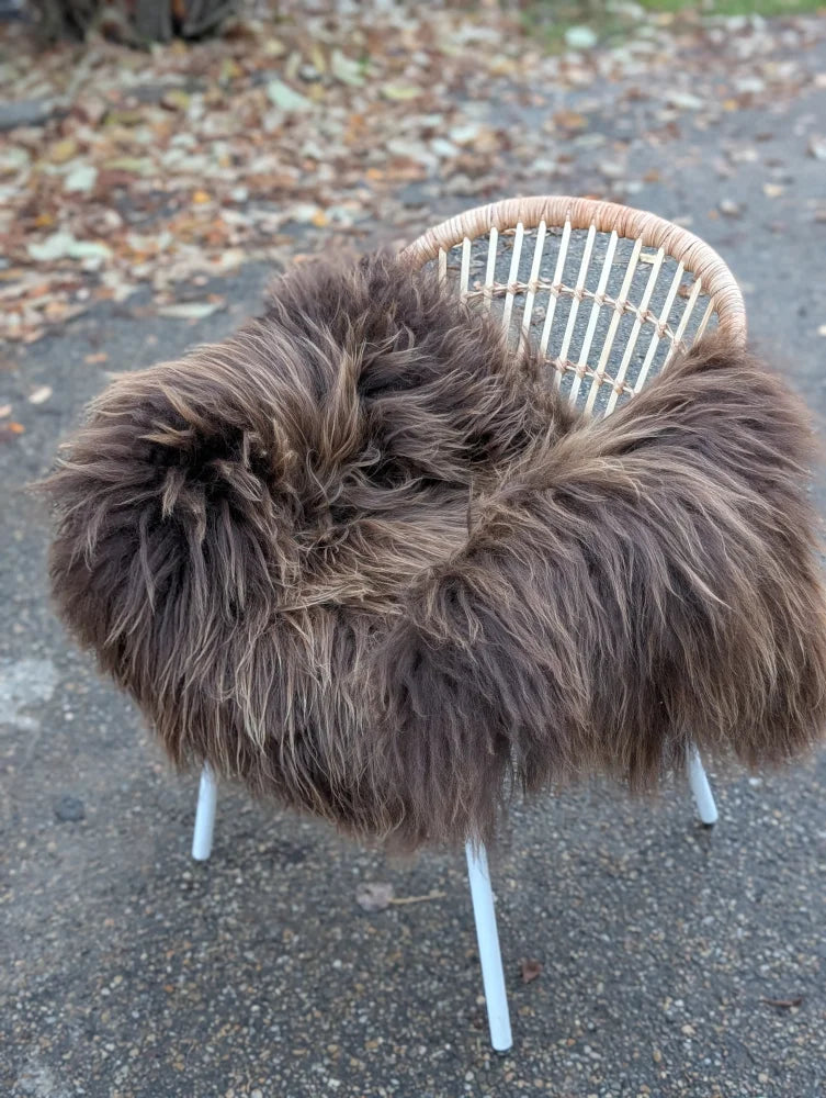 A plush dark rusty icelandic sheepskin throw draped over a white wicker chair showcasing long wool icelandic texture