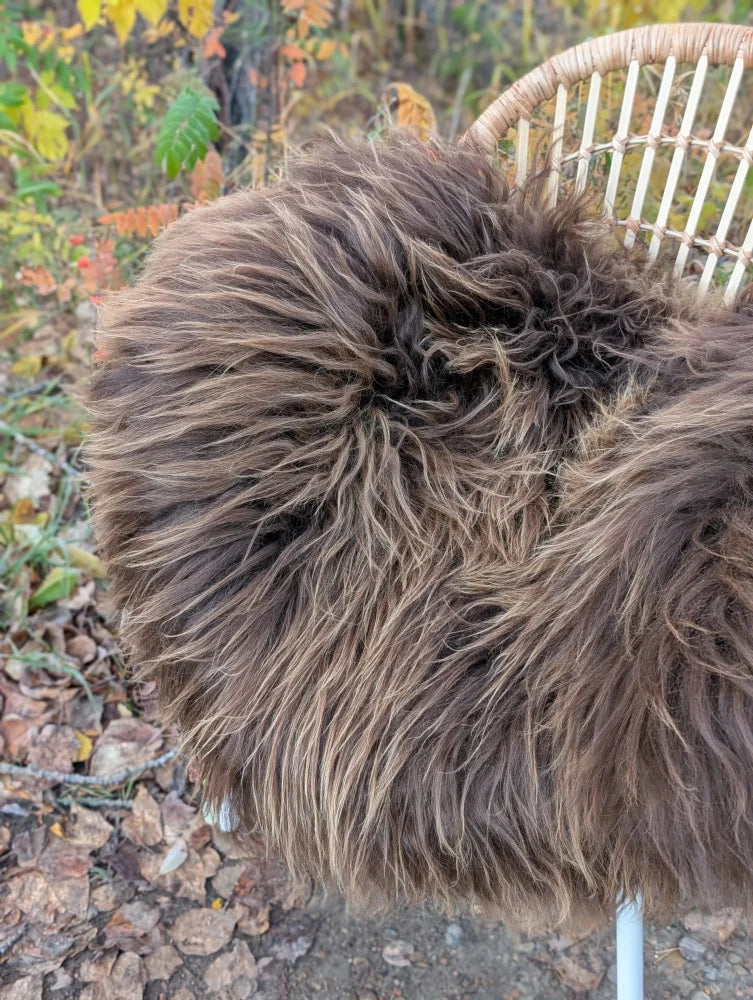 A massive natural bronze icelandic sheepskin wool throw draped over a wicker chair for cozy warmth