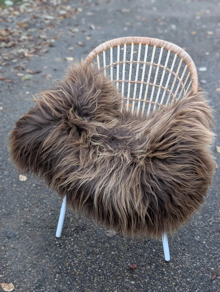 A cozy thick dark rusty icelandic sheepskin throw draped over a modern white wicker chair for extra warmth