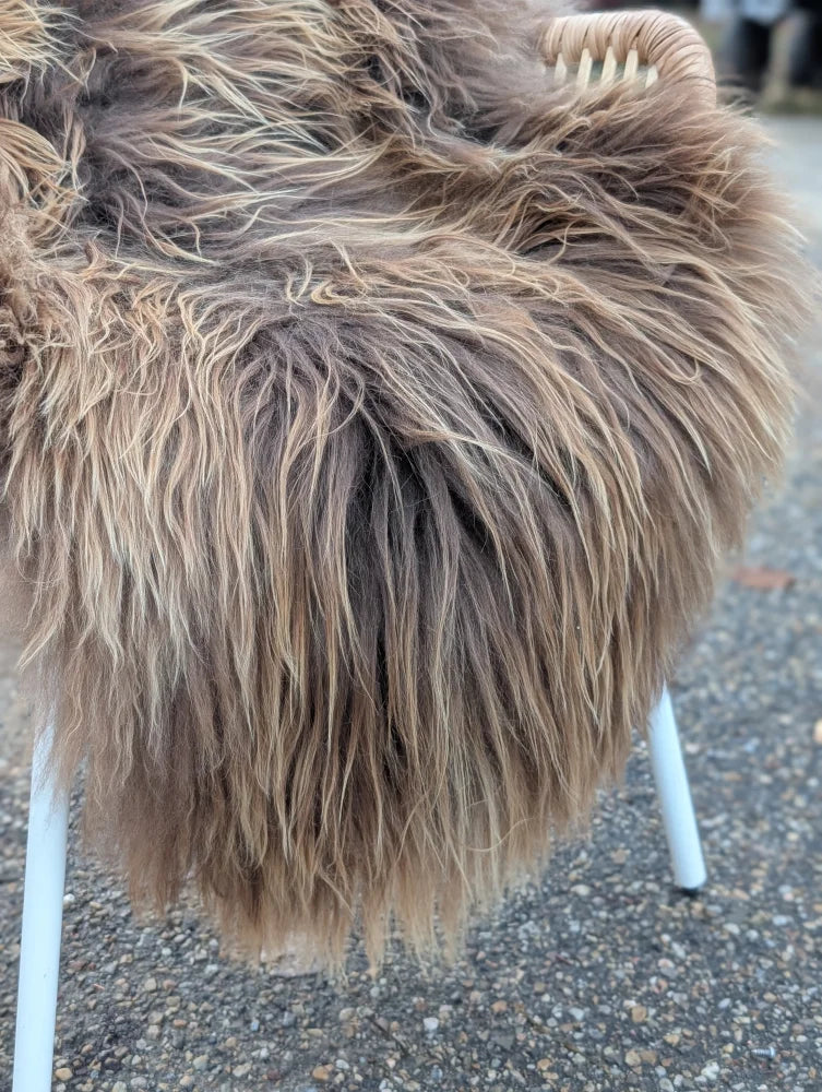 A plush long wool icelandic sheepskin throw in dark rusty bronze tones draped over a white chair