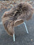A cozy thick brown dark rusty icelandic sheepskin throw draped over a wicker chair with white metal legs