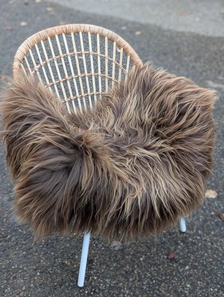 A cozy dark rusty icelandic sheepskin throw with long wool draped over a wicker chair with white metal legs