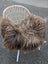 A cozy dark rusty icelandic sheepskin throw with long wool draped over a wicker chair with white metal legs