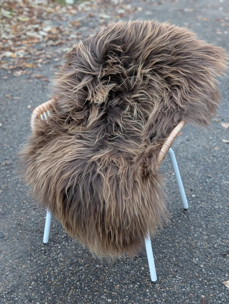 A plush dark rusty icelandic sheepskin rug with long wool draped over a modern white metal chair with wicker arms