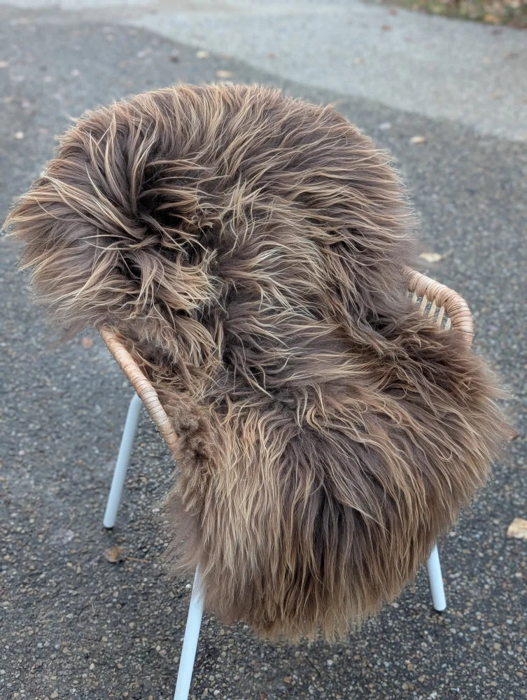 A plush long wool icelandic sheepskin rug in dark rusty bronze draped over a white wicker chair