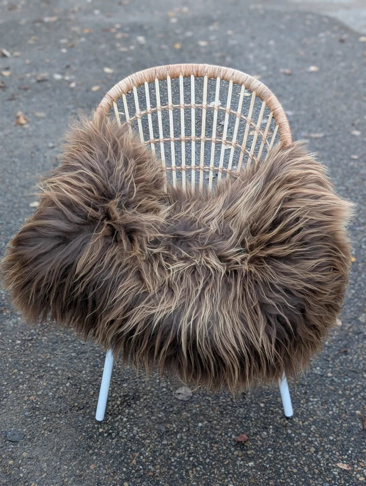 A cozy thick dark rusty icelandic long wool icelandic sheepskin draped over a woven wicker chair with white legs