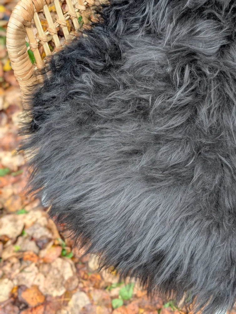 A plush dark gray long wool icelandic sheepskin throw resting on a woven wicker chair for cozy use