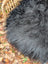 A plush dark gray long wool icelandic sheepskin throw resting on a woven wicker chair for cozy use