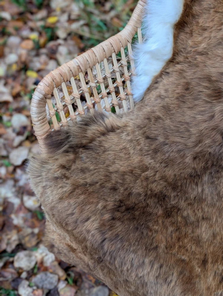 A plush brown wool icelandic sheepskin shortwool throw draped over a woven wicker chair arm