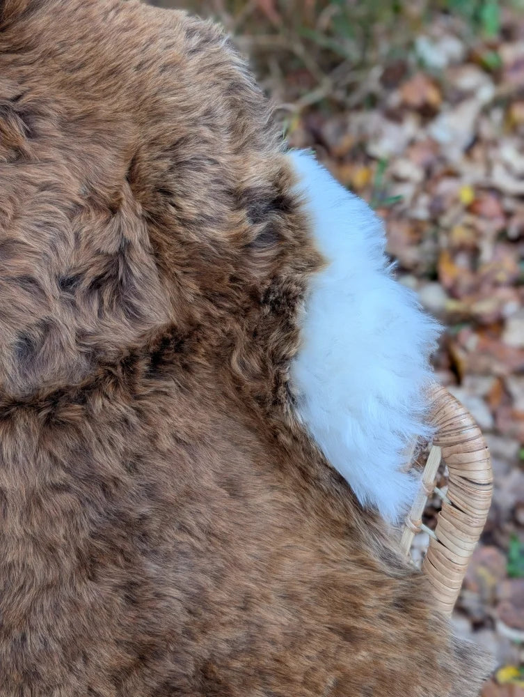 A fluffy brown and white icelandic sheepskin shortwool rug with a woven wicker handle perfect for cozy spaces