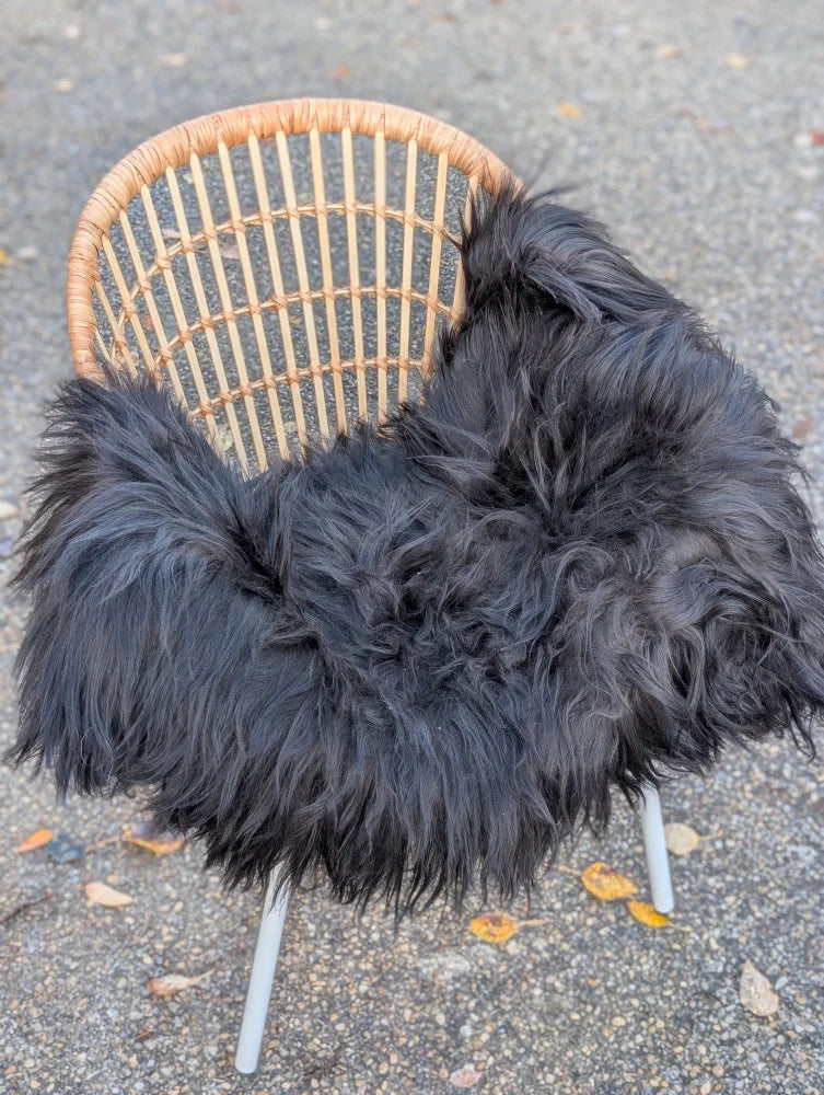 Black fluffy long wool icelandic sheepskin throw draped over wicker chair for cozy decor