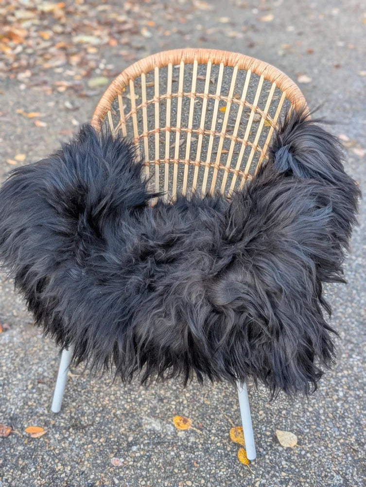 A cozy black icelandic sheepskin long wool throw draped over a woven rattan chair with slender white legs