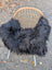 A cozy black icelandic sheepskin long wool throw draped over a woven rattan chair with slender white legs