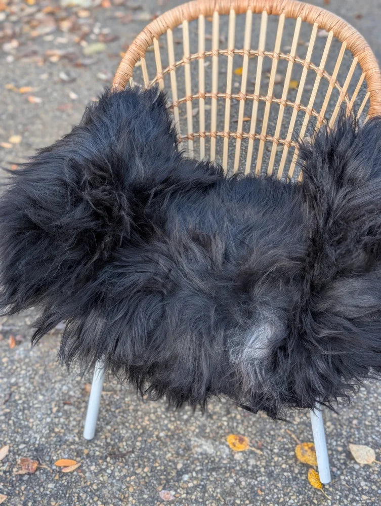 Black fluffy long wool icelandic sheepskin throw draped over wicker chair for cozy natural decor