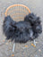Black long wool icelandic sheepskin chair cover draped over wicker chair with white metal legs