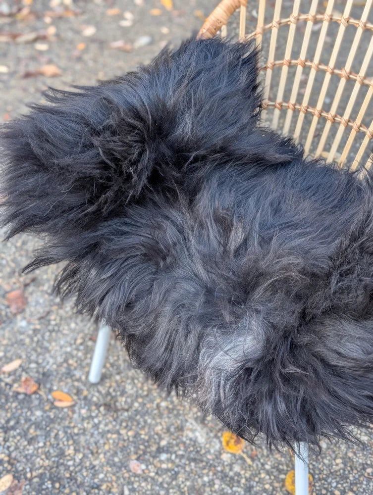A plush dark gray long wool icelandic sheepskin throw draped over a wicker chair for cozy use