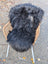 Black thickly textured icelandic sheepskin rug with long wool draped over a wicker chair for cozy decor