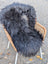 Black thick fluffy long wool icelandic sheepskin rug draped over wicker chair in natural black color